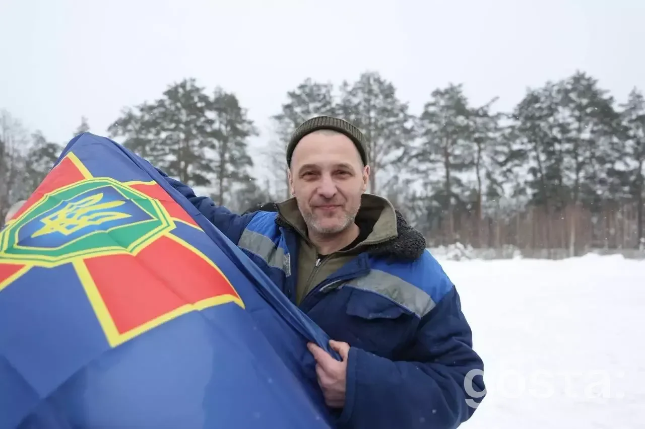 Військовослужбовець з українським прапором на фоні засніжених дерев, повернення 157 захисників додому.