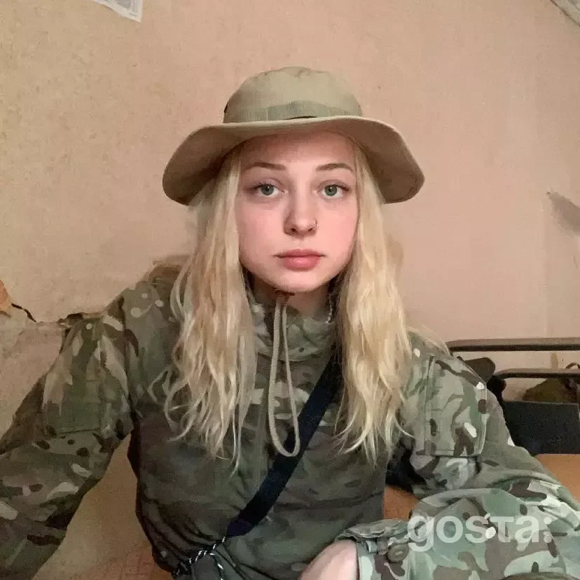 На фото зображено молода жінка у камуфляжі, зосереджена та готова до служби.