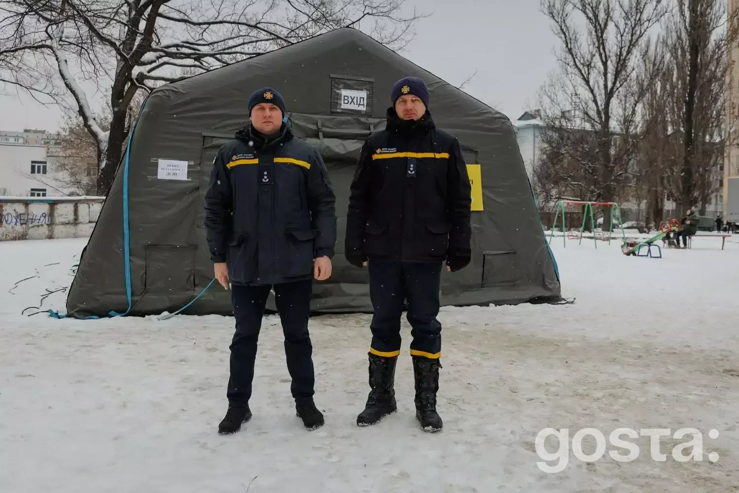 На фото два рятувальники стоять перед швидкомонтованим пунктом обігріву на засніженій території.