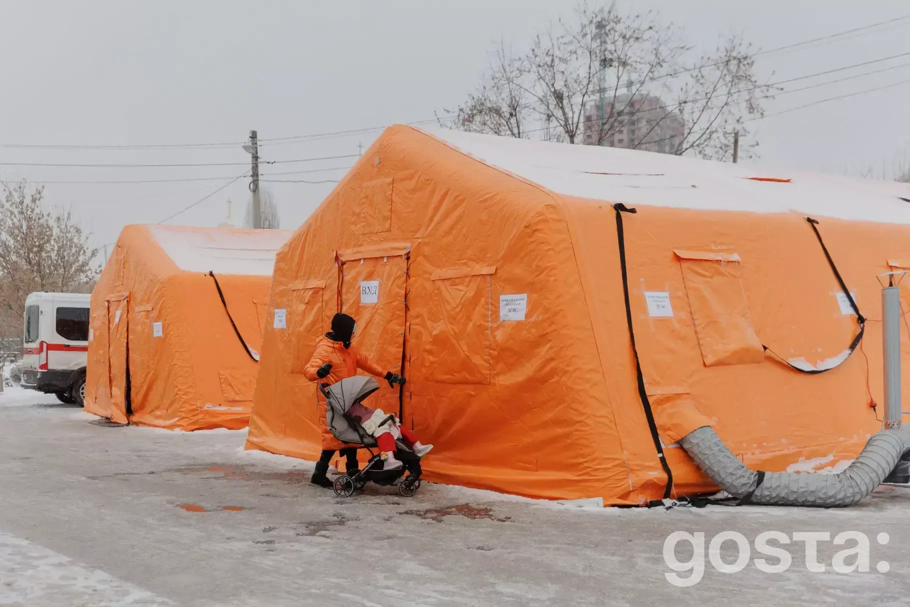 Жінка з дитячим візочком входить в оранжевий намет Пункту Незламності ДСНС України в зимовому Києві.