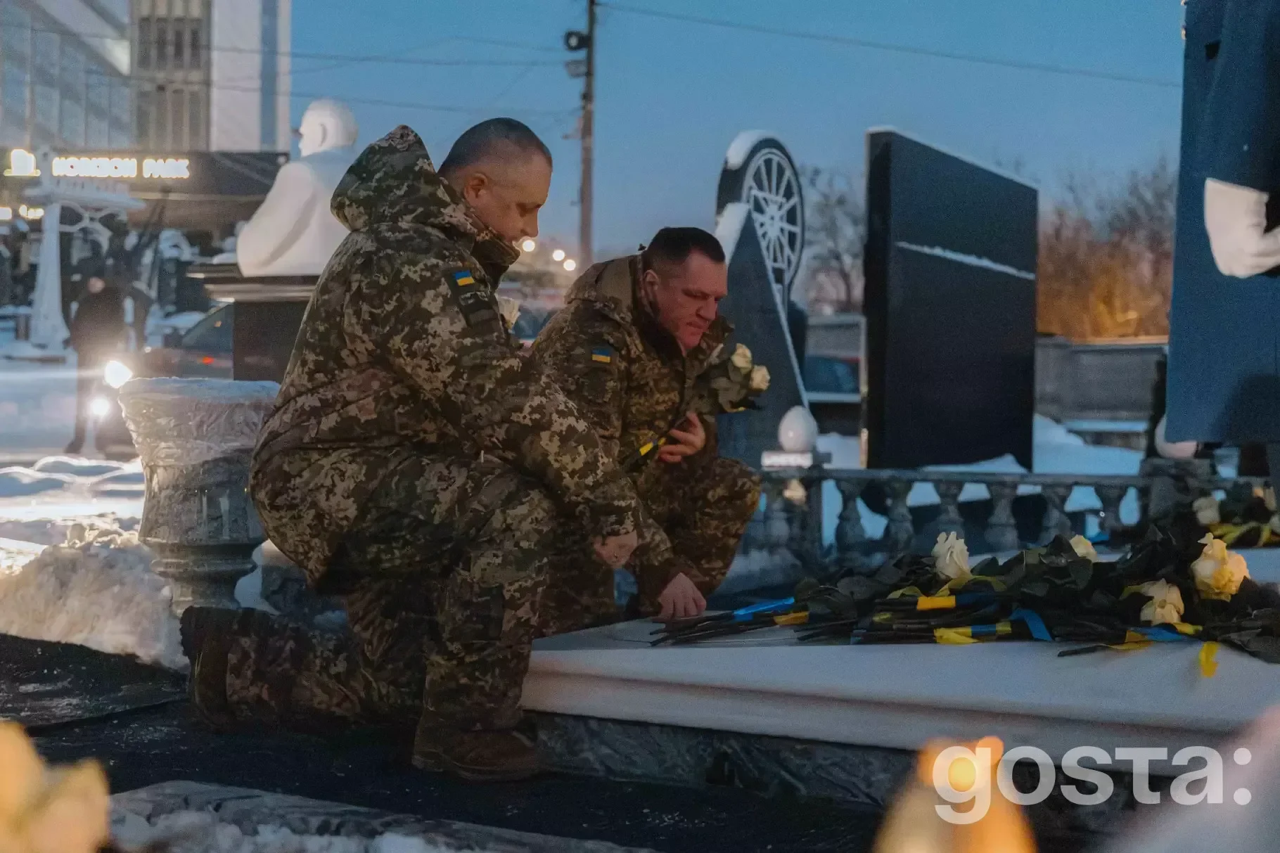 Двоє чоловіків у військовій формі вшановують пам'ять загиблих на Байковому кладовищі, покладаючи квіти до меморіалу.