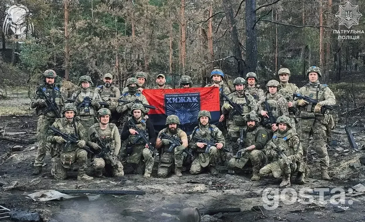 На зображенні група військовослужбовців стоїть в лісі з прапором.
