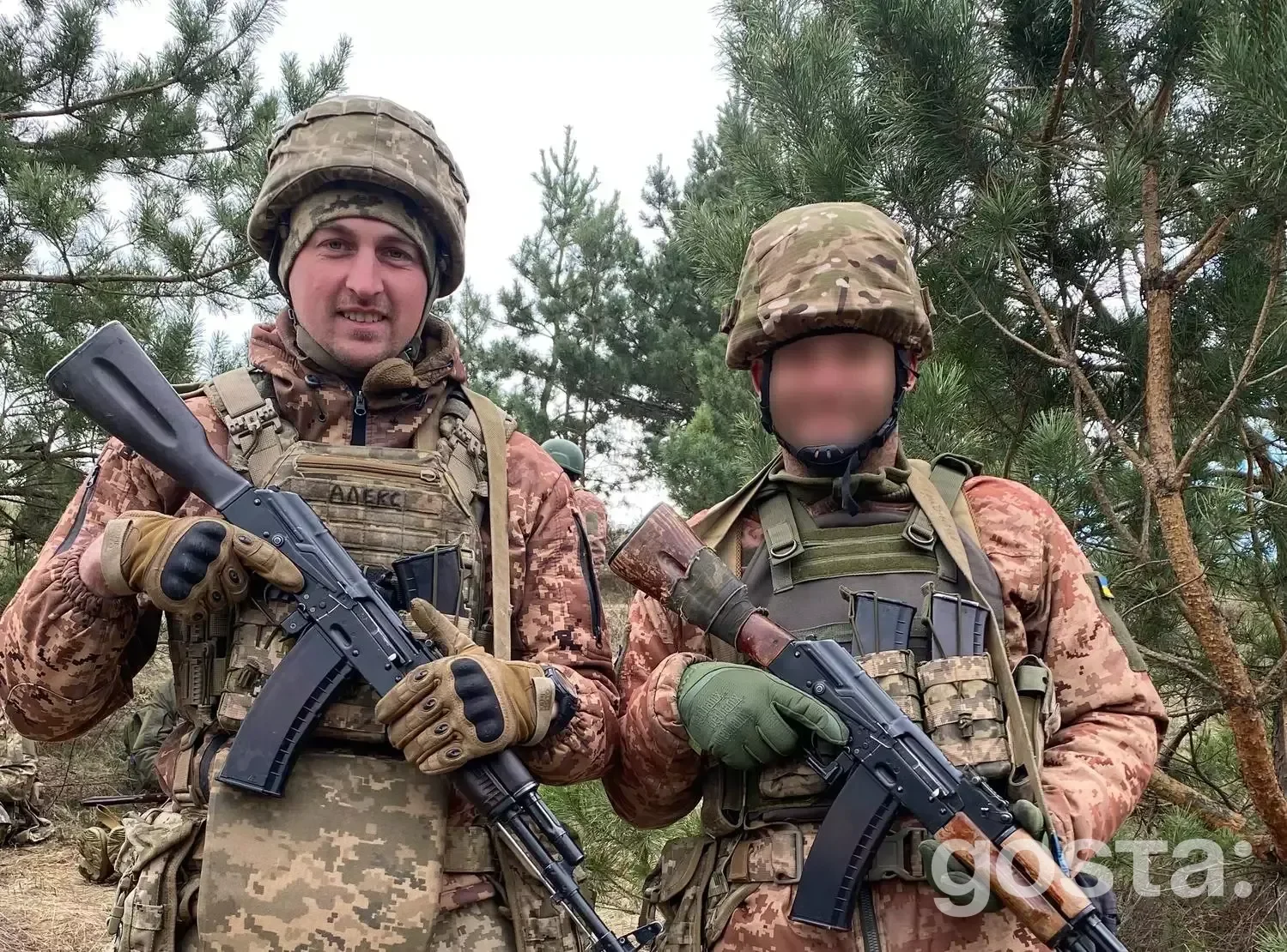 На фото двоє військовослужбовців у камуфляжній формі з автоматами стоять серед дерев.