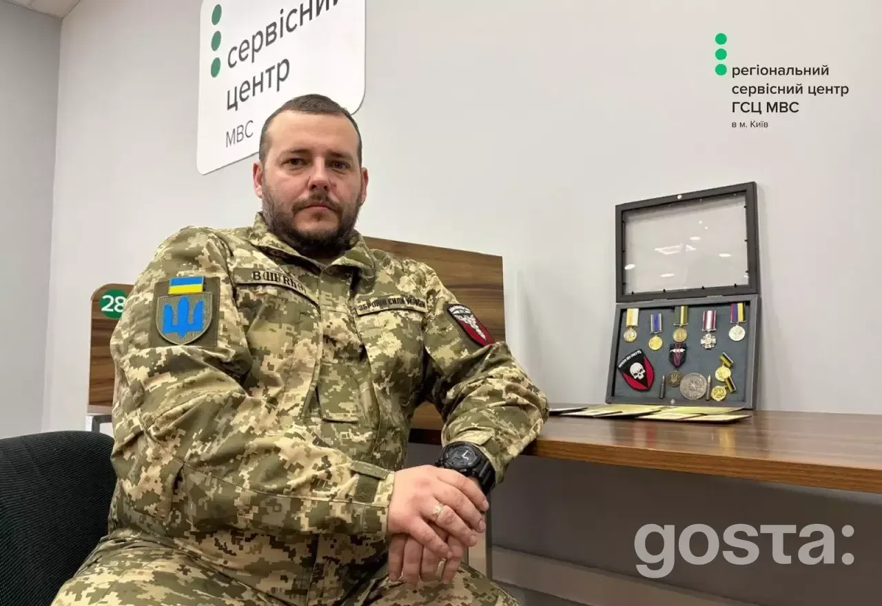 Ветеран у військовій формі сидить у сервісному центрі МВС, поруч з нагородами, демонструючи служіння державі.