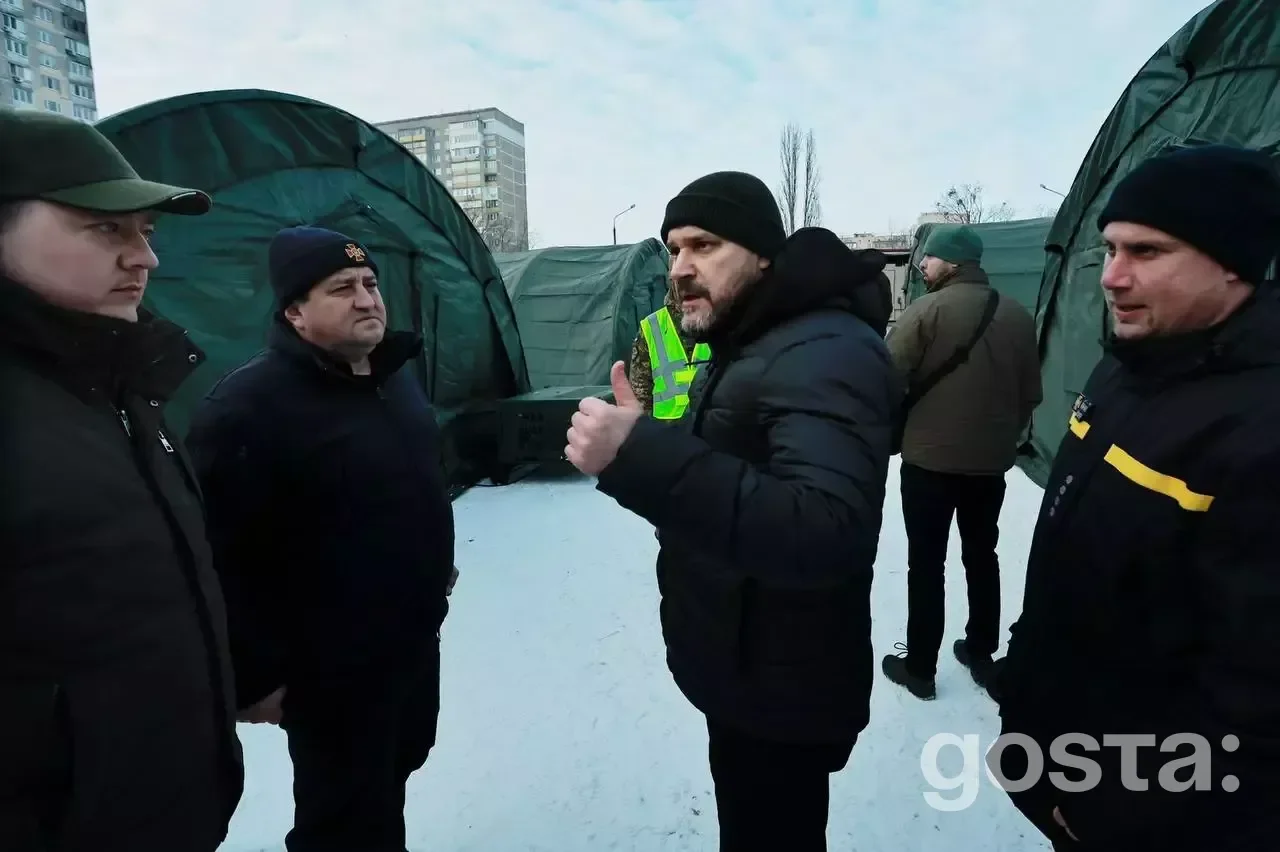 Група людей обговорює розгортання наметів обігріву на фоні міських будівель, з метою допомоги в умовах надзвичайної ситу