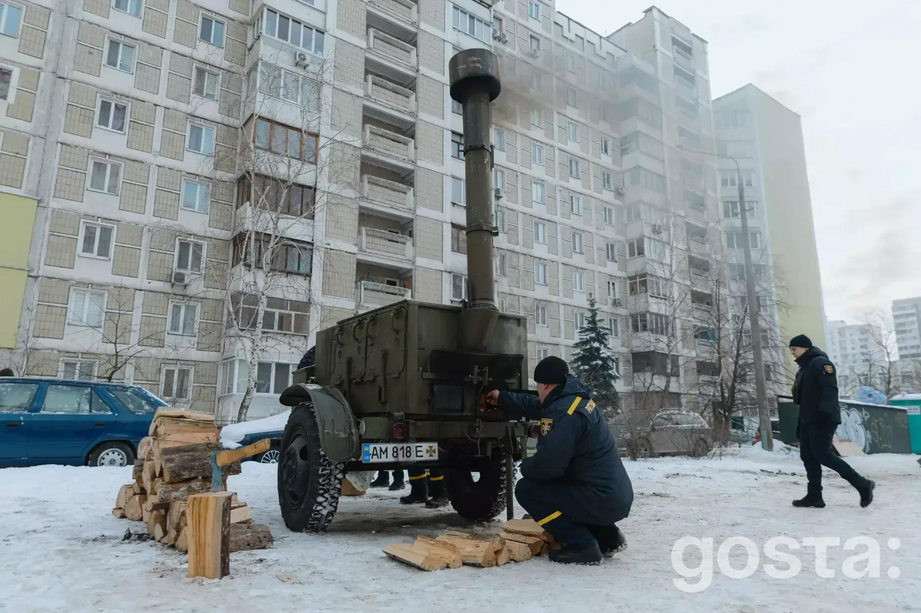 Рятувальник біля мобільної пічки ДСНС у пункті обігріву на фоні багатоповерхівки в зимовий час у Києві.