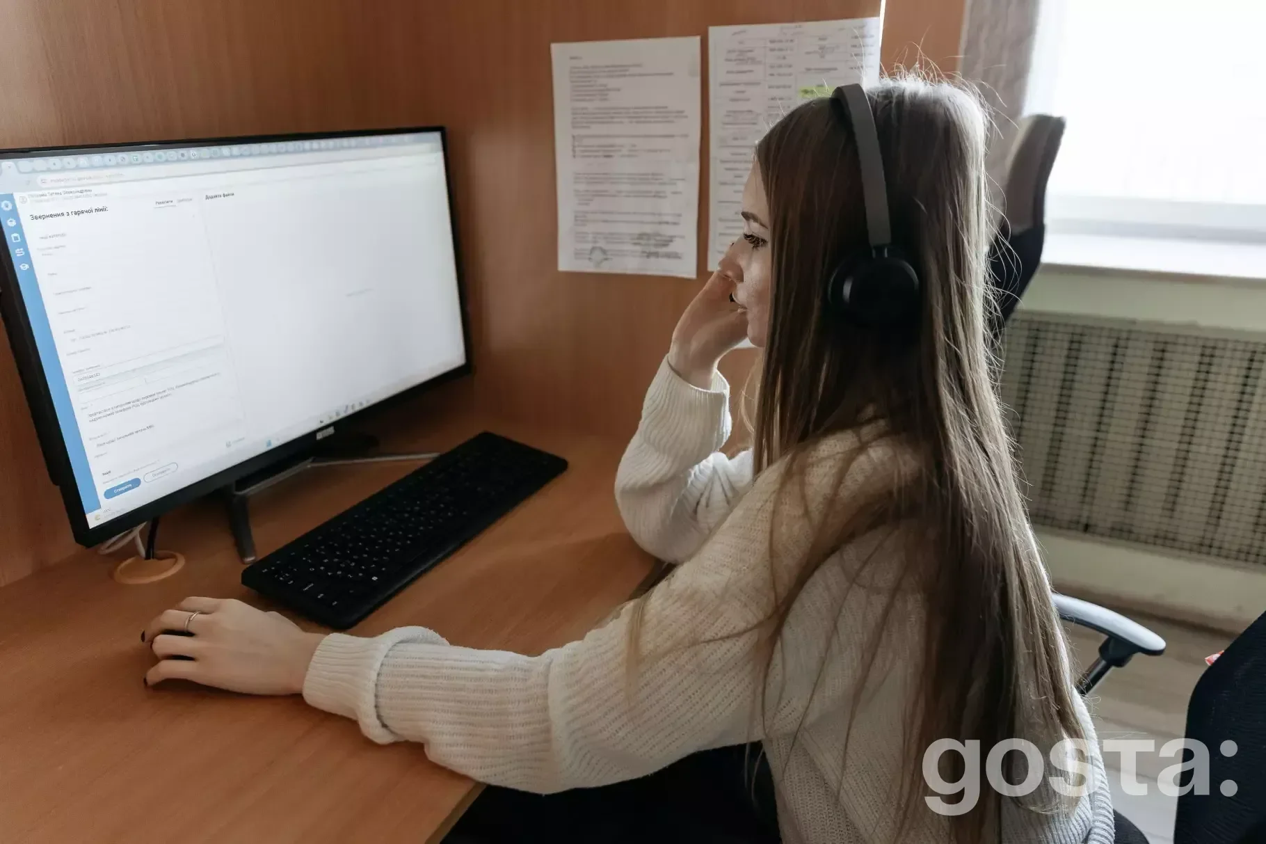 Жінка працює оператором контакт-центру, використовуючи гарнітуру та комп'ютер у приміщенні гарячої лінії МВС України.