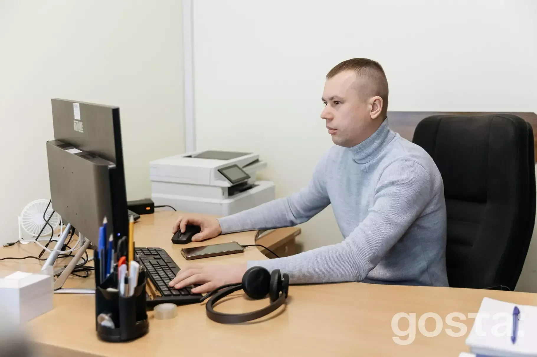 Чоловік працює за комп'ютером в офісі, бездротові навушники на столі, займається обробкою дзвінків для контактного центр