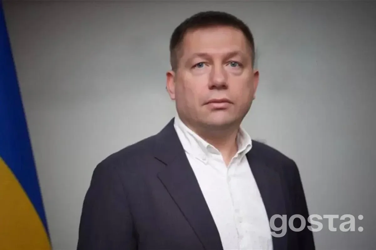 На фото зображено чоловіка в офіційному одязі на фоні прапора України.