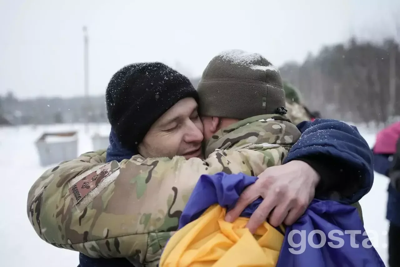 Двоє чоловіків у військовій формі обіймаються, тримаючи український прапор на снігу.
