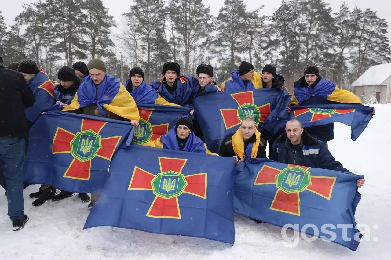 Група військовослужбовців із прапорами України, радіють поверненню додому після обміну полоненими.