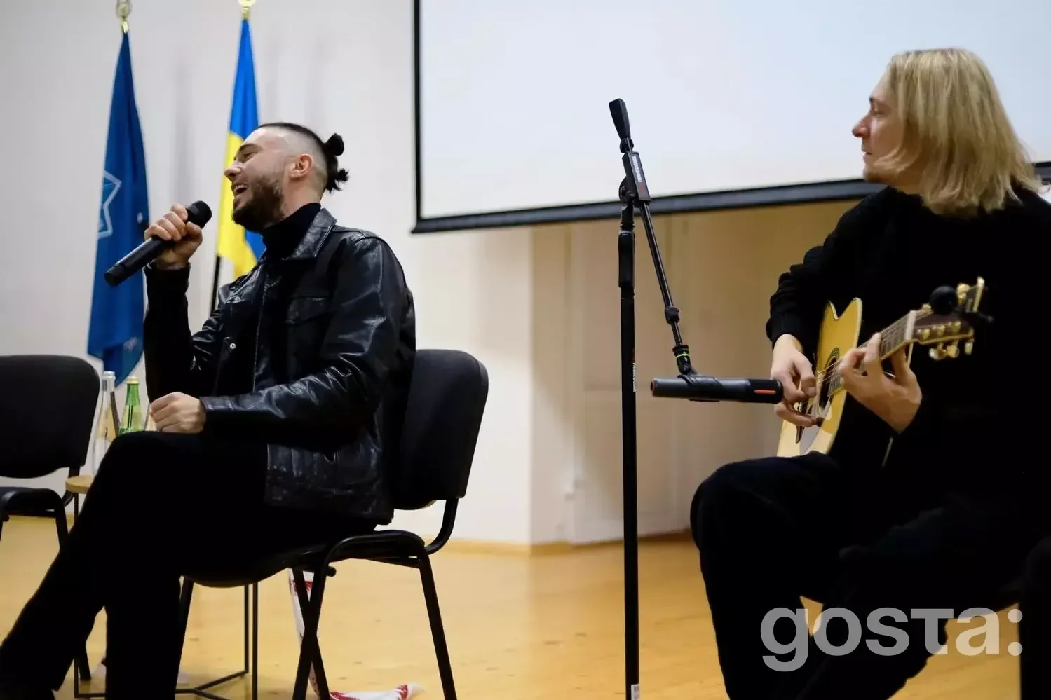 На сцені музиканти гурту «Антитіла» виступають перед ліцеїстами у залі, поруч український прапор.