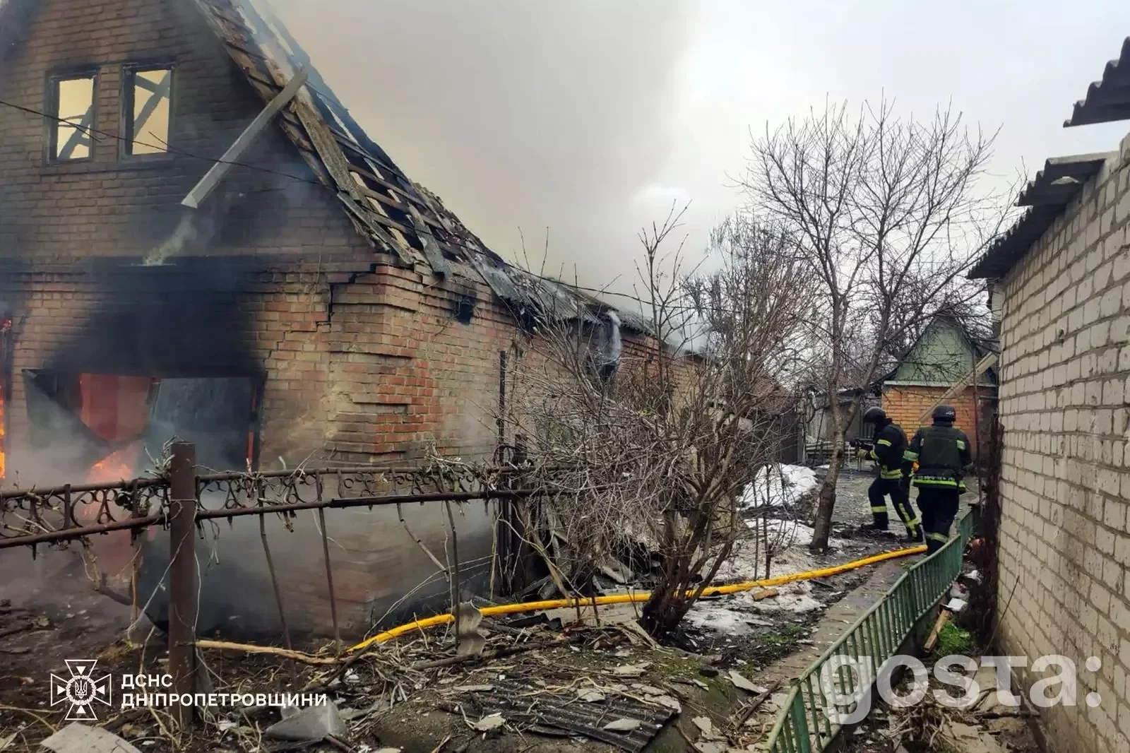 Пожежники гасять палаючий будинок після російського обстрілу в Україні, пошкоджено дах і стіни, дим здіймається в небо.