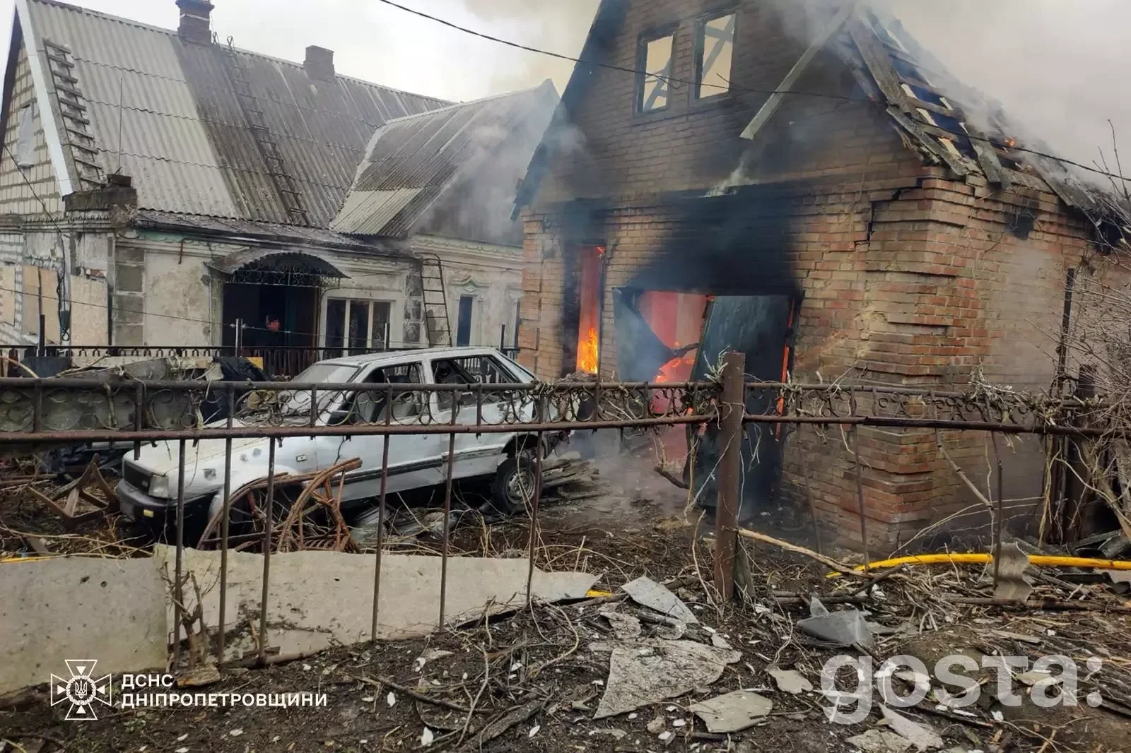 Зруйнований будинок після обстрілів у Дніпропетровщині, пошкоджений автомобіль, дим та полум'я видно з вікна.