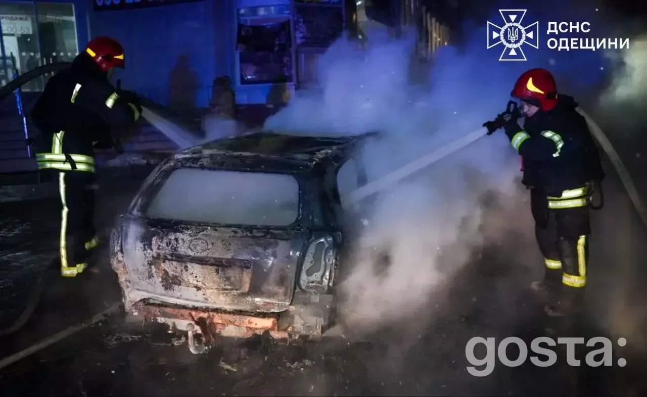 Рятувальники гасять палаючий автомобіль під час обстрілів в Україні; нічний інцидент, дим та вода, пожежники в дії.